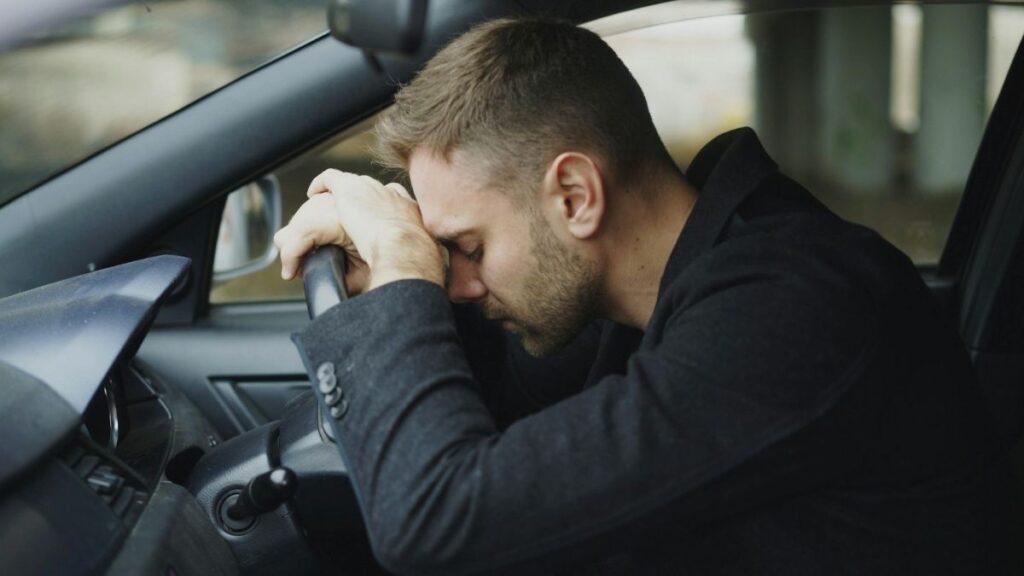 Exhausted man resting his head on the steering wheel after a long commute