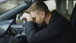 Exhausted man resting his head on the steering wheel after a long commute