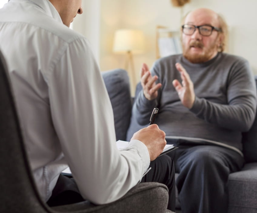 Man gesturing as he talks with a therapist who takes notes during a free initial consultation