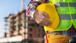 Male tradesperson in a hi-vis vest holding a hard hat at a construction site