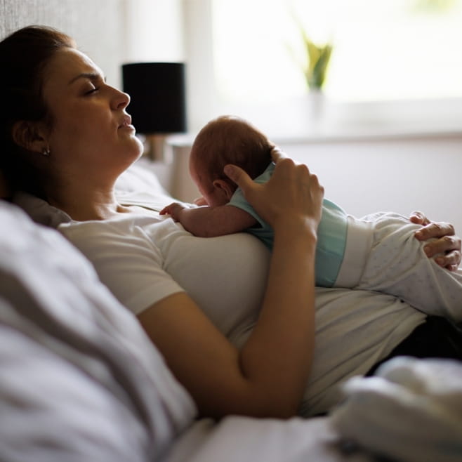 Exhausted new mother holding her newborn in the early weeks, when baby blues are common
