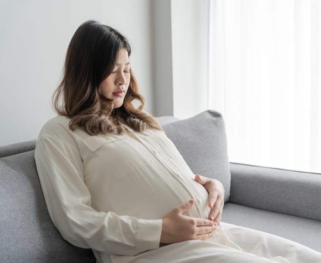 Pregnant woman sitting quietly on a sofa with her hands on her bump, low in mood